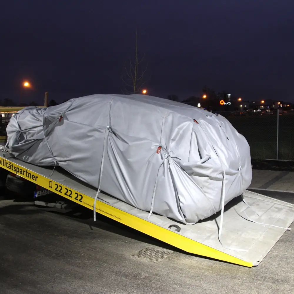 Fahrzeug mit VLITEX Abdeckung auf einem Abschleppwagen bei Nacht.